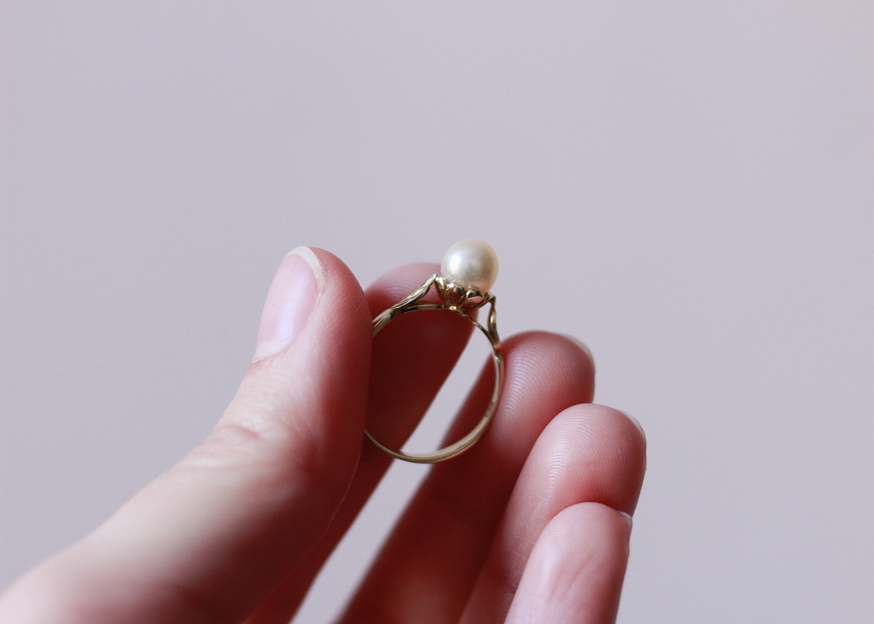 image of a left hand showing the top side of a gold ring with a pearl on it, as the pearl is positioned on top