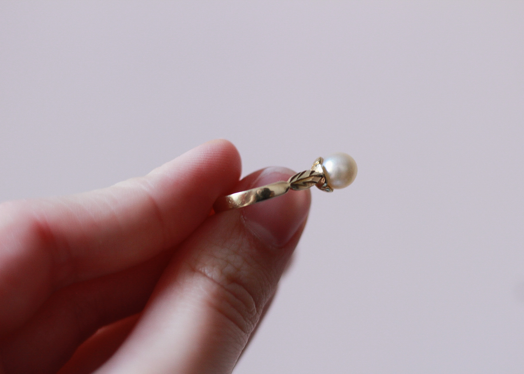 image of a left hand showing the leaf detail of the left side of a gold ring with a pearl on it