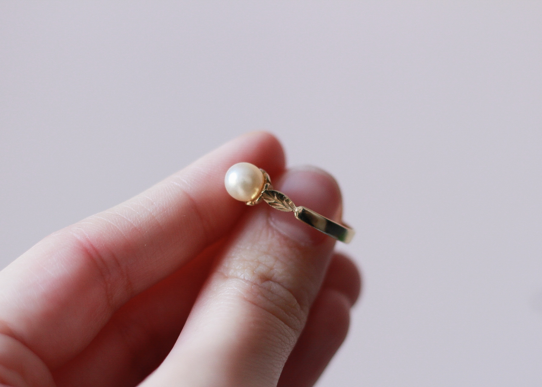 image of a left hand showing the leaf detail on the right side of a gold ring with a pearl on it