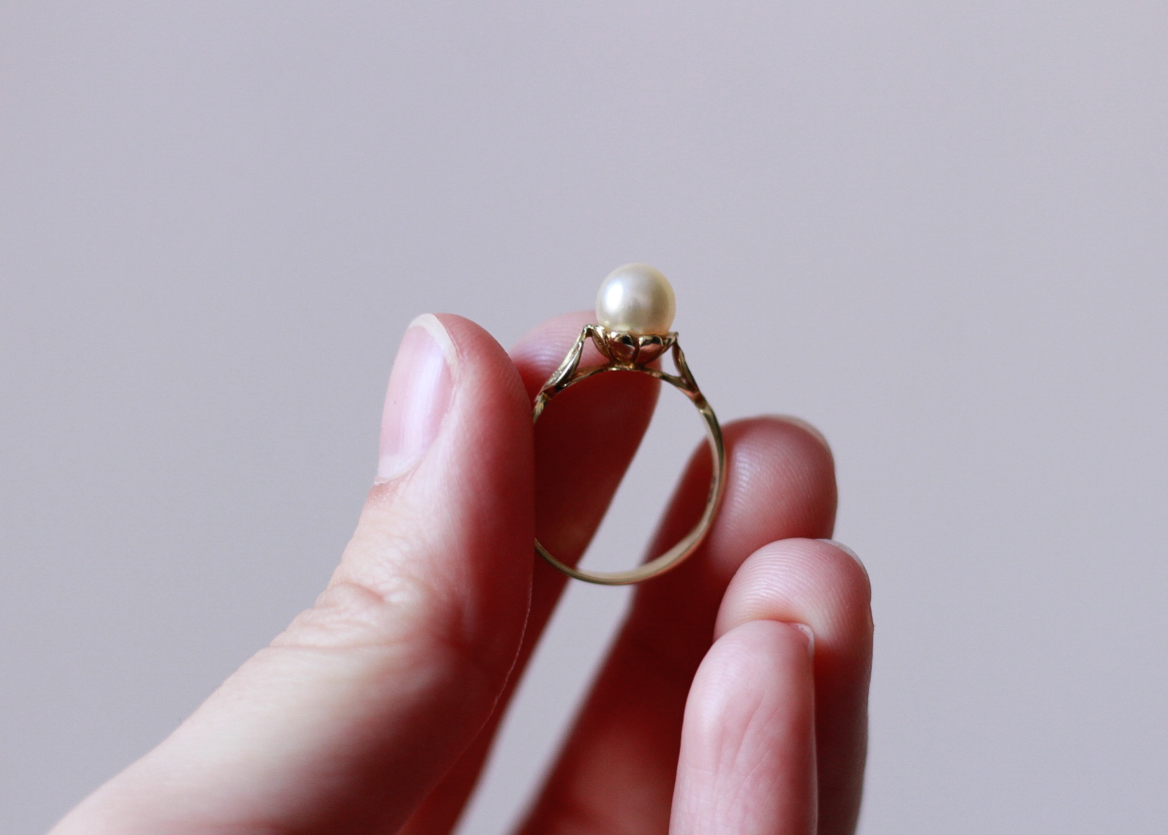 image of a left hand showing the bottom side of a gold ring with a pearl on it, as the pearl is positioned on top